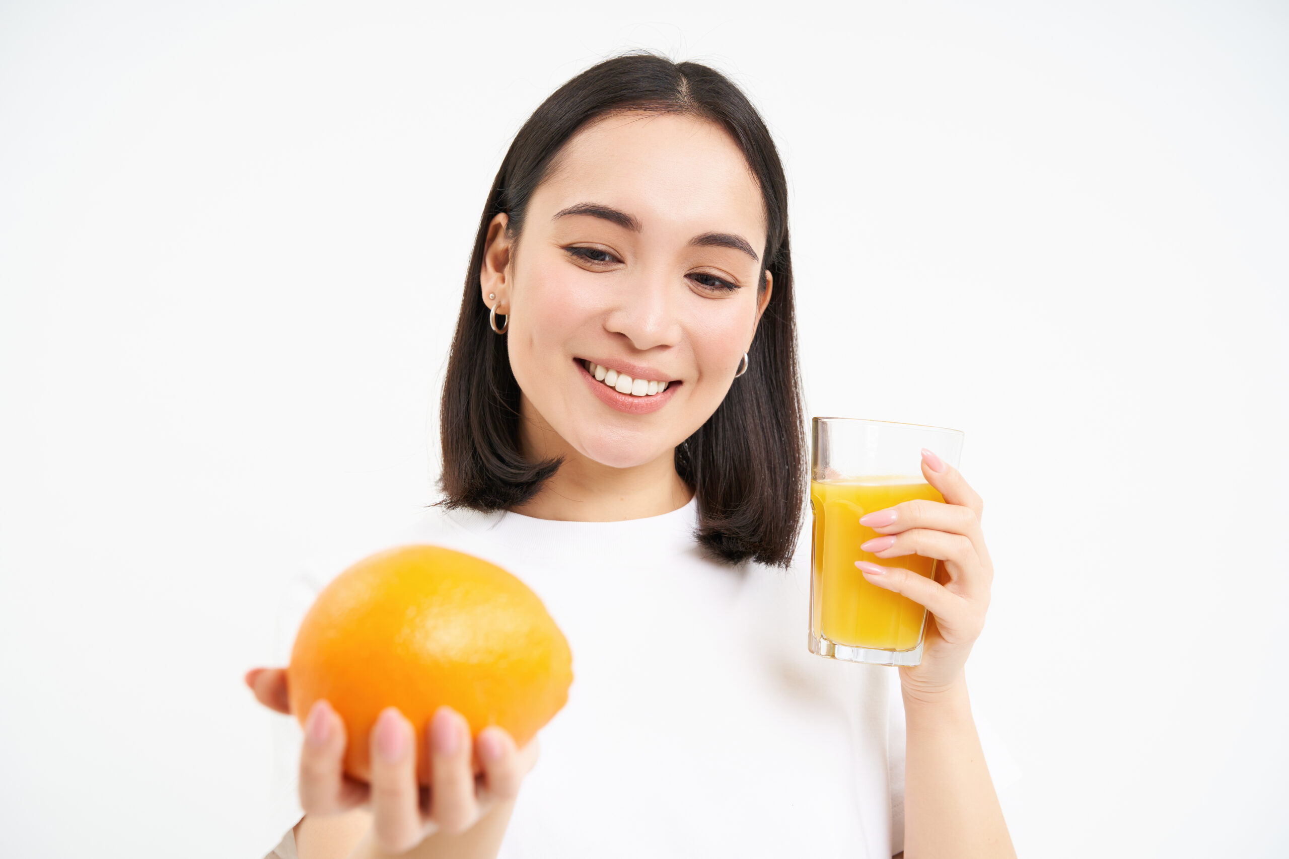 Portrait of smiling brunette woman, squeeze one glass of fresh juice from orange and looking happy, has healthy drink, white background