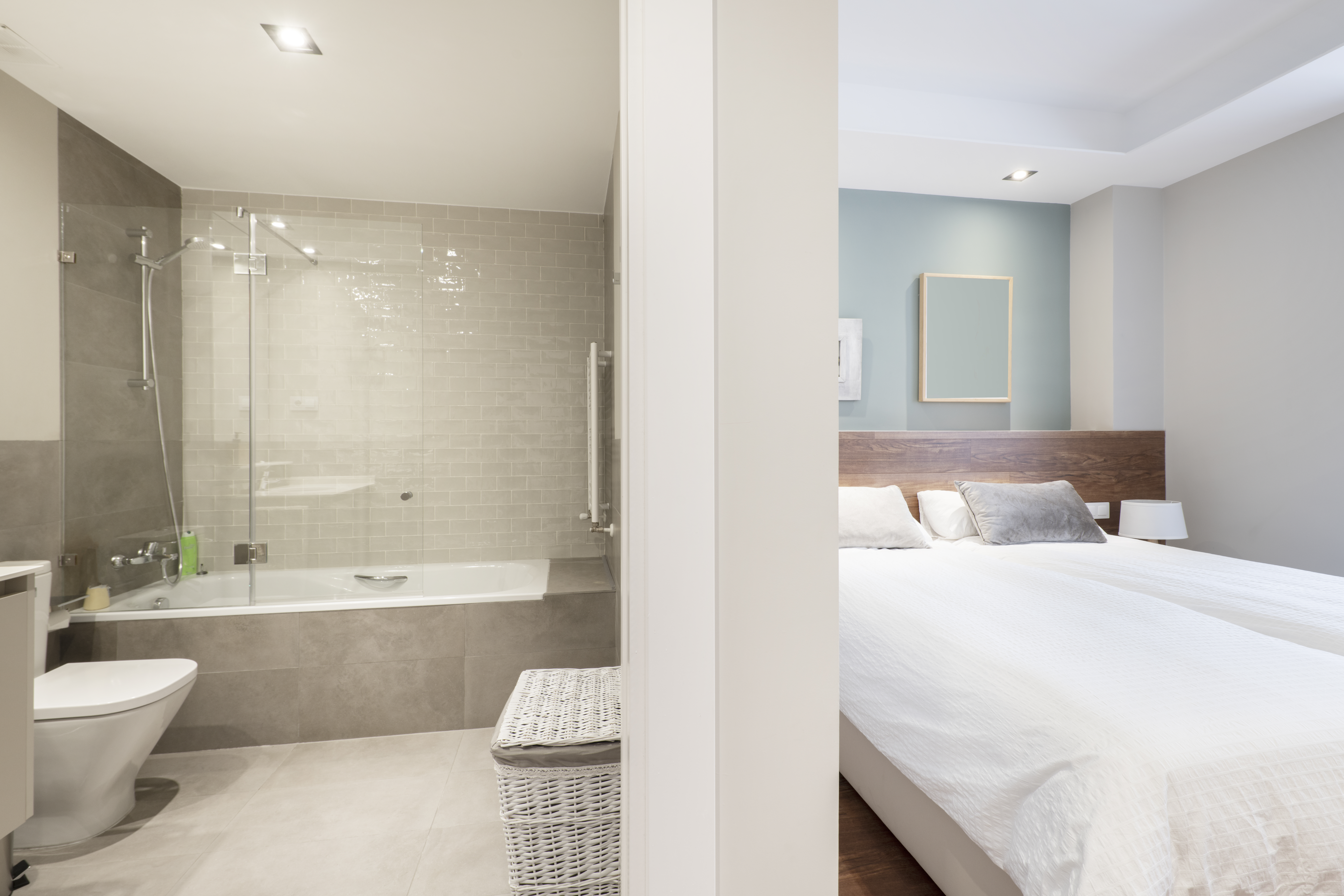 Bathroom with bathtub with glass partitions, gray tiles and bedr