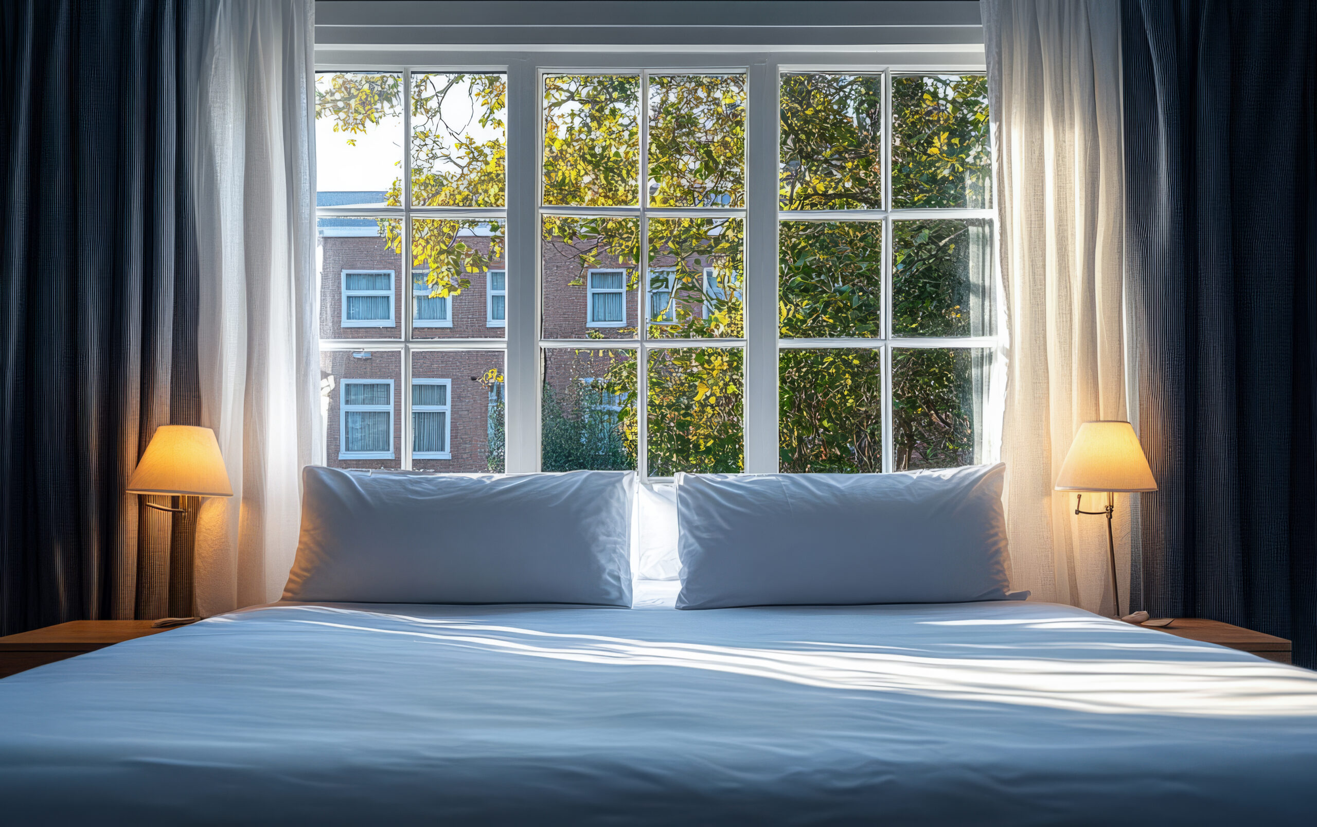 Cozy bedroom with large window showing sunlight and trees outside during daytime