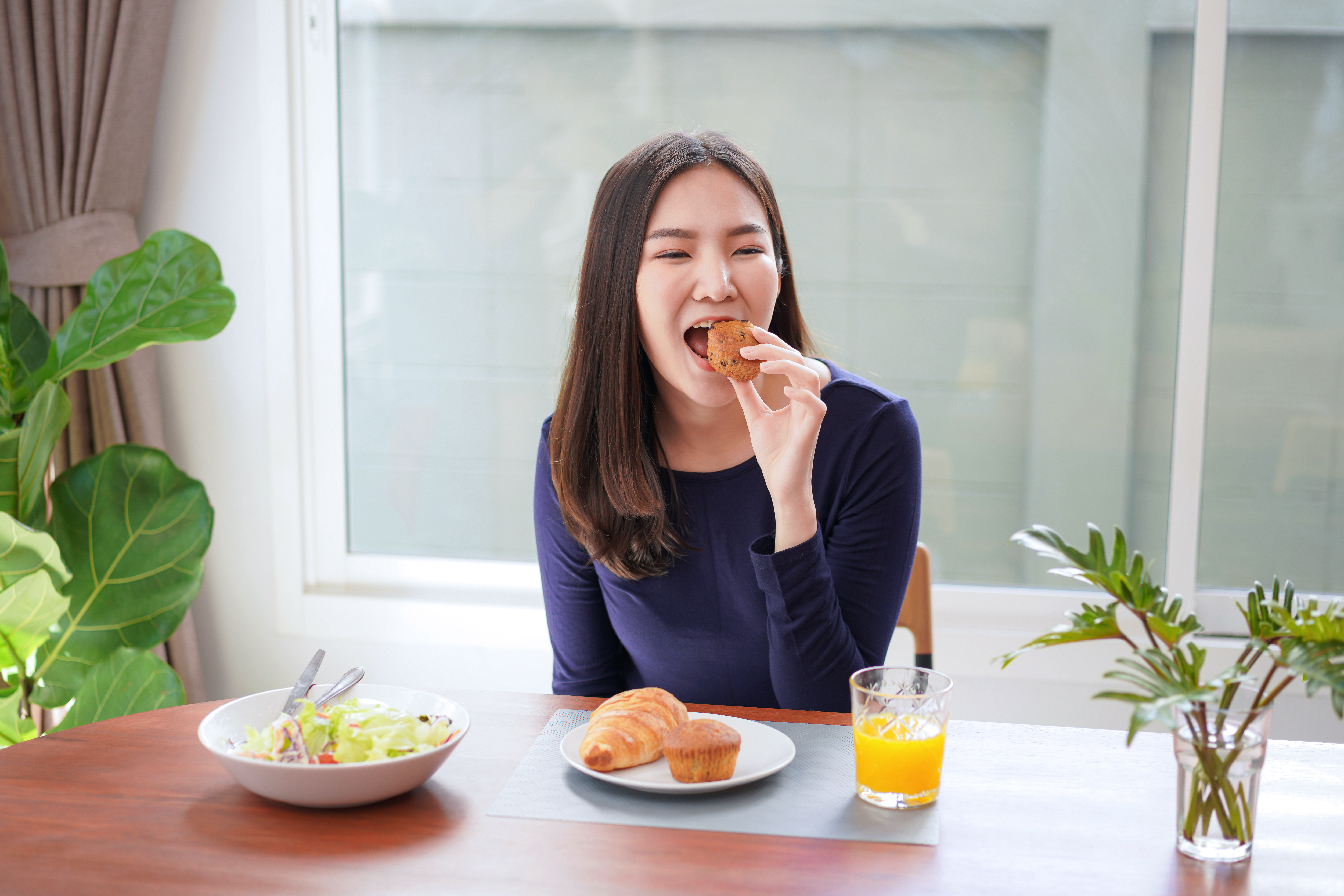 Young asian woman eating bread with a glass of fresh orange juic