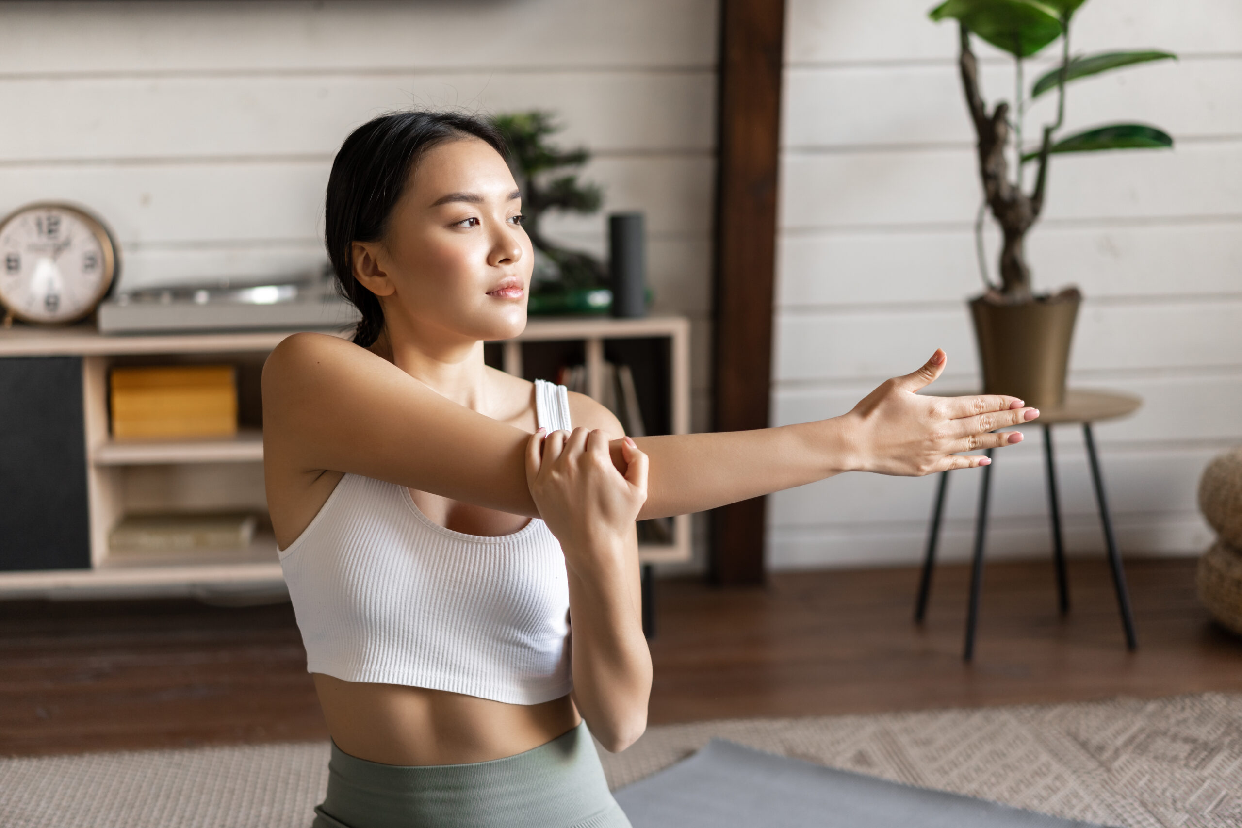 Young sporty woman in activewear, doing stretching, morning yoga or workout at home, sitting on floor mat