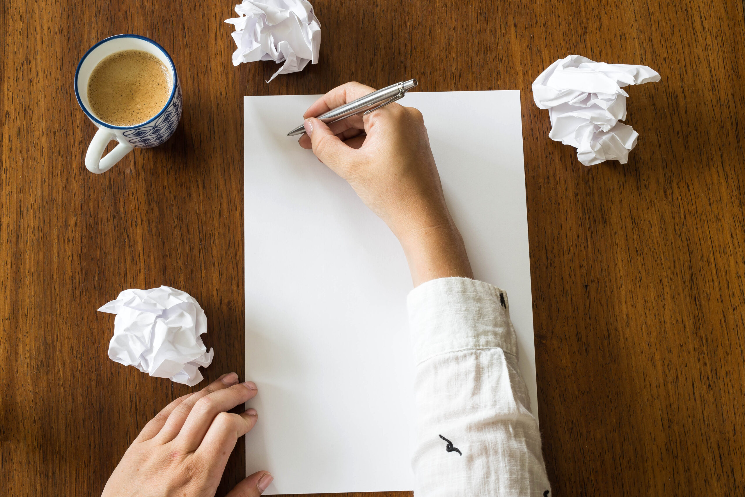 Blank sheet of paper and pen on bright wooden office desk with hands of a person