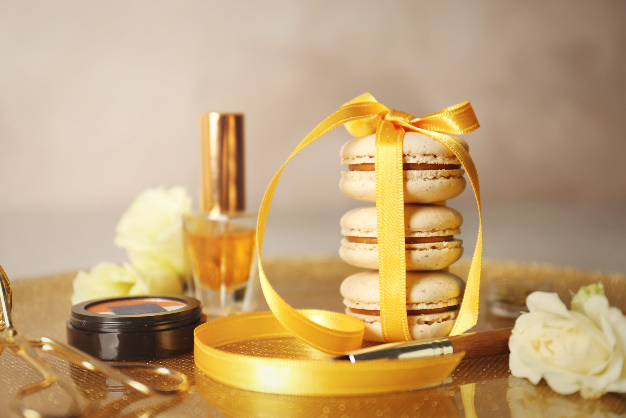 Tied with ribbon macaroons and beauty accessories on golden surface